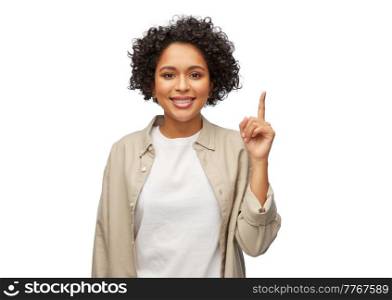 people, ethnicity and portrait concept - happy smiling woman in shirt pointing finger up over white background. portrait of smiling woman pointing finger up