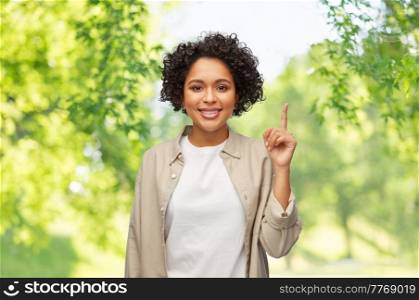 people, ethnicity and portrait concept - happy smiling woman in shirt pointing finger up over green natural background. woman pointing finger up over natural background