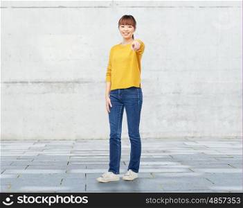 people, ethnicity, choice and gesture concept - happy asian young woman pointing finger on you over stone wall background