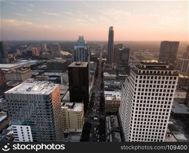 People exit downtown Austin as the sun hits the horizon through a maze of tall buildings