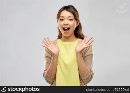 people, expression and emotion concept - happy amazed asian young woman over grey background. happy asian woman over grey background