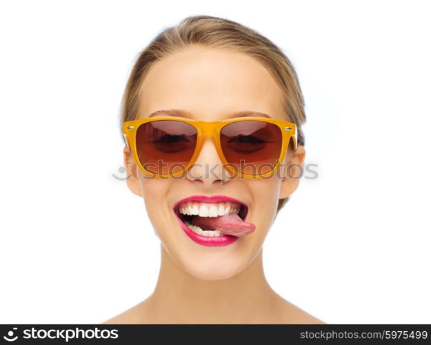 people, expression, joy and fashion concept - smiling young woman in sunglasses with pink lipstick on lips showing tongue
