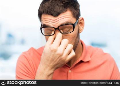 people, eyesight, stress, overwork and business concept - tired man in eyeglasses rubbing his eyes at home or work
