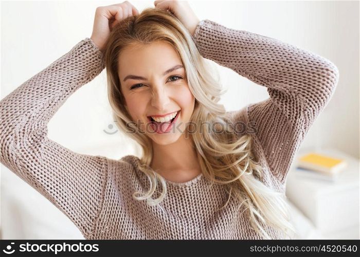 people, facial expression and emotion concept - happy young woman or teenage girl having fun and showing tongue at home