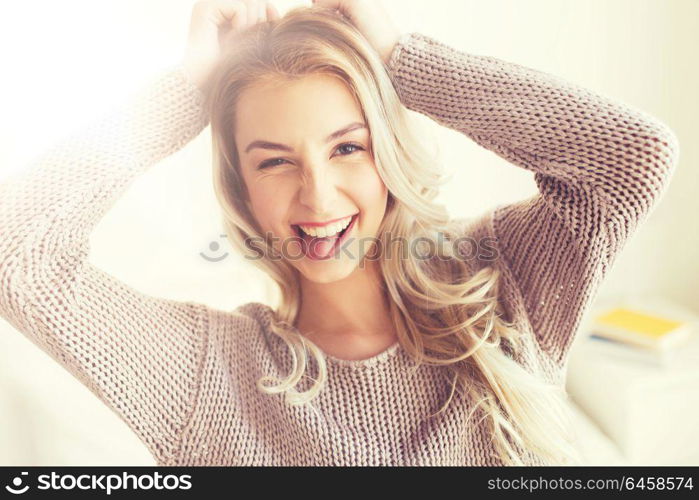 people, facial expression and emotion concept - happy young woman or teenage girl having fun and showing tongue at home. happy young woman or teenage girl at home