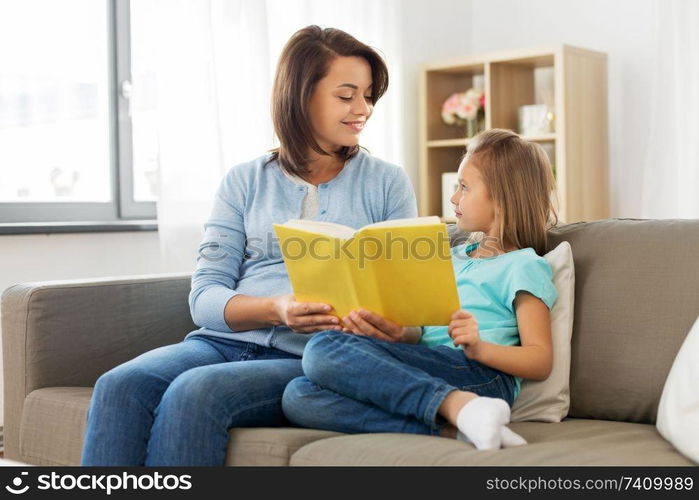 people, family and education concept - happy daughter with mother reading book at home. happy girl with mother reading book at home