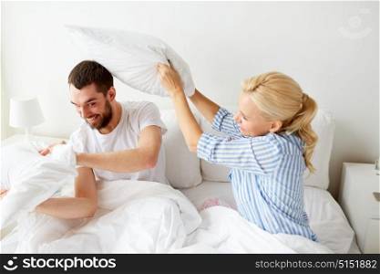 people, family and fun concept - happy couple having pillow fight in bed at home. happy couple having pillow fight in bed at home