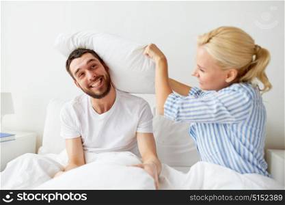 people, family and fun concept - happy couple having pillow fight in bed at home. happy couple having pillow fight in bed at home