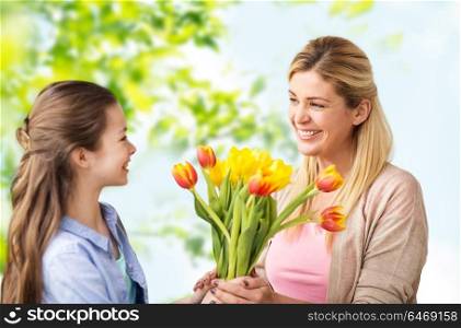 people, family and holidays concept - happy daughter giving tulip flowers to her mother over green natural background. happy daughter giving flowers to mother
