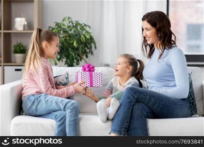 people, family and holidays concept - happy girl giving birthday present to younger sister at home. girl giving present to younger sister at home