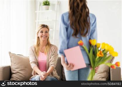 people, family and holidays concept - happy girl giving tulip flowers and greeting card to her mother at home. happy girl giving flowers to mother at home. happy girl giving flowers to mother at home
