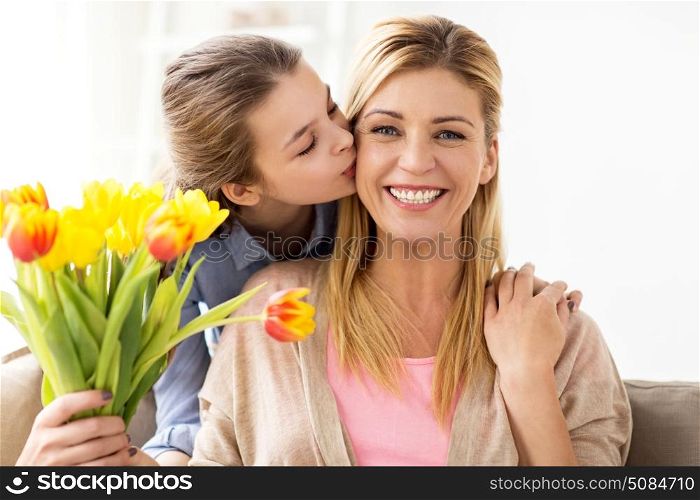 people, family and holidays concept - happy girl giving tulip flowers and kissing her mother at home. happy girl giving flowers to mother at home. happy girl giving flowers to mother at home
