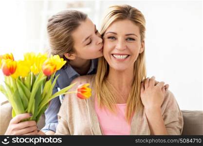 people, family and holidays concept - happy girl giving tulip flowers and kissing her mother at home. happy girl giving flowers to mother at home. happy girl giving flowers to mother at home