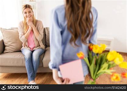 people, family and holidays concept - happy girl giving tulip flowers and greeting card to her mother at home. happy girl giving flowers to mother at home
