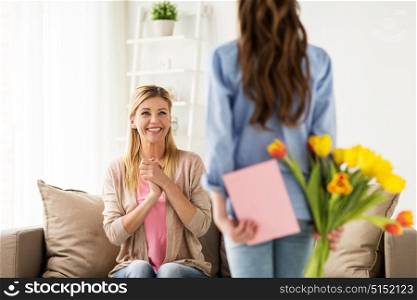 people, family and holidays concept - happy girl giving tulip flowers and greeting card to her mother at home. happy girl giving flowers to mother at home