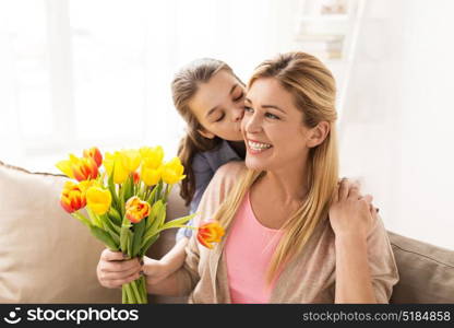 people, family and holidays concept - happy girl giving tulip flowers and kissing her mother at home. happy girl giving flowers to mother at home