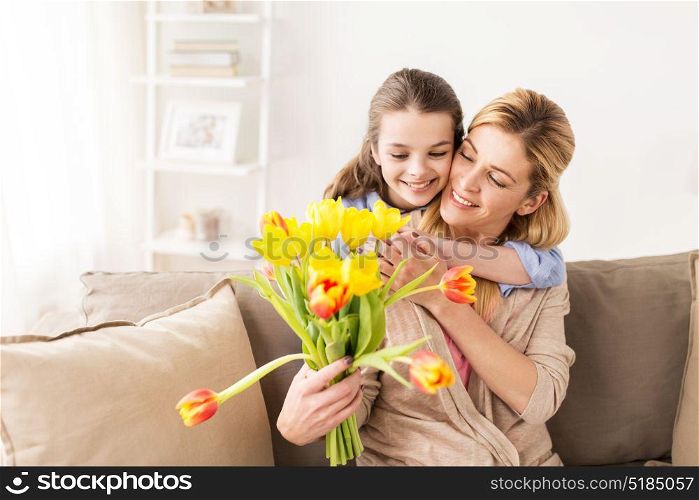 people, family and holidays concept - happy girl giving tulip flowers and hugging her mother at home. happy girl giving flowers to mother at home