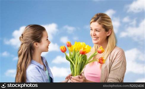 people, family and holidays concept - happy girl giving tulip flowers to her mother over blue sky and clouds background. happy girl giving flowers to mother over blue sky