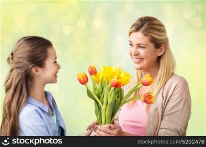 people, family and holidays concept - happy girl giving tulip flowers to her mother over lights background. happy girl giving flowers to mother over lights