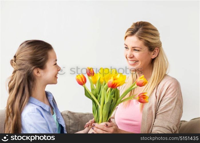 people, family and holidays concept - happy girl giving tulip flowers to her mother at home. happy girl giving flowers to mother at home