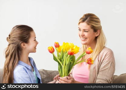 people, family and holidays concept - happy girl giving tulip flowers to her mother at home. happy girl giving flowers to mother at home