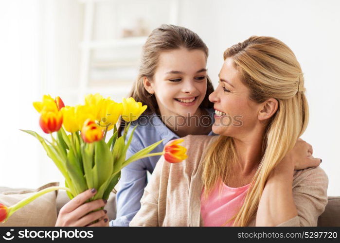 people, family and holidays concept - happy girl giving tulip flowers to her mother at home. happy girl giving flowers to mother at home