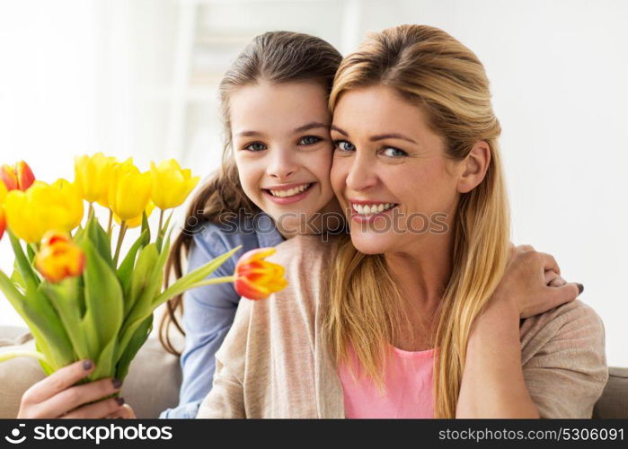 people, family and holidays concept - happy girl giving tulip flowers to her mother at home. happy girl giving flowers to mother at home