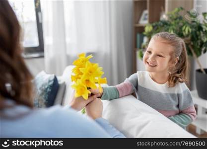 people, family and holidays concept - happy little daughter giving daffodil flowers to mother at home. happy daughter giving daffodil flowers to mother