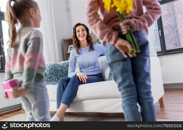 people, family and holidays concept - two daughters giving flowers and birthday present to happy mother at home. daughters giving flowers and gift to happy mother