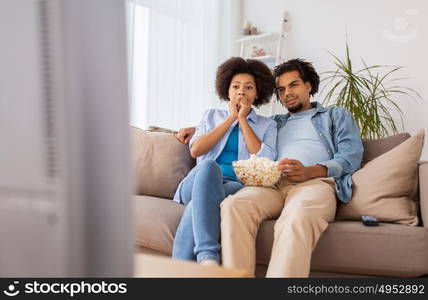 people, family and leisure concept - couple with popcorn watching tv at home. couple with popcorn watching tv at home