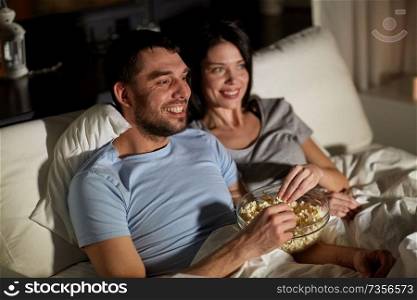 people, family and leisure concept - couple with popcorn watching tv at night at home. couple with popcorn watching tv at night at home