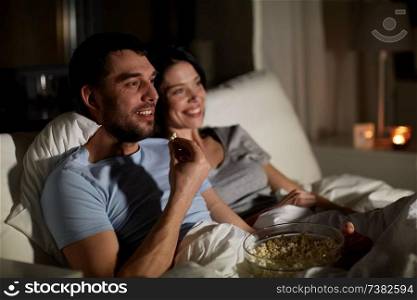 people, family and leisure concept - couple with popcorn watching tv at night at home. couple with popcorn watching tv at night at home