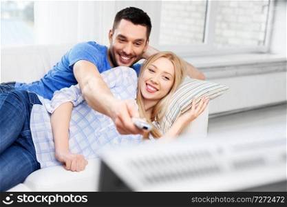 people, family and leisure concept - happy smiling couple watching tv at home. happy smiling couple watching tv at home
