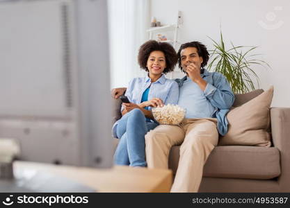 people, family and leisure concept - smiling couple with popcorn watching tv at home. smiling couple with popcorn watching tv at home