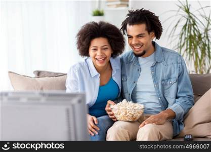 people, family and leisure concept - smiling couple with popcorn watching tv at home. smiling couple with popcorn watching tv at home