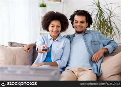 people, family and leisure concept - smiling couple with remote watching tv at home. smiling couple with remote watching tv at home