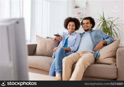 people, family and leisure concept - smiling couple with remote watching tv at home. smiling couple with remote watching tv at home