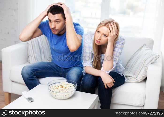 people, family and leisure concept - upset couple with popcorn watching tv at home. upset couple with popcorn watching tv at home