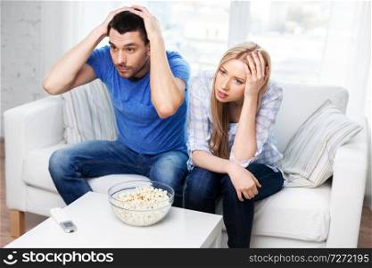 people, family and leisure concept - upset couple with popcorn watching tv at home. upset couple with popcorn watching tv at home