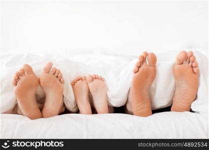 people, family and morning concept - bare soles or feet of parents and child in bed at home