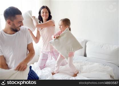 people, family and morning concept - happy child with parents having pillow fight in bed at home