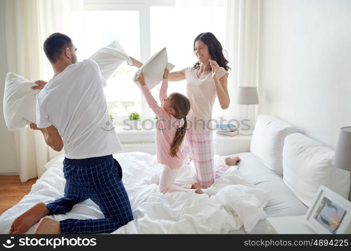 people, family and morning concept - happy child with parents having pillow fight in bed at home