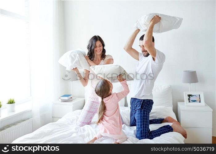 people, family and morning concept - happy child with parents having pillow fight in bed at home. happy family having pillow fight in bed at home