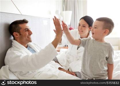 people, family and morning concept - happy child with parents in bed at home or hotel room. happy family in bed at home or hotel room