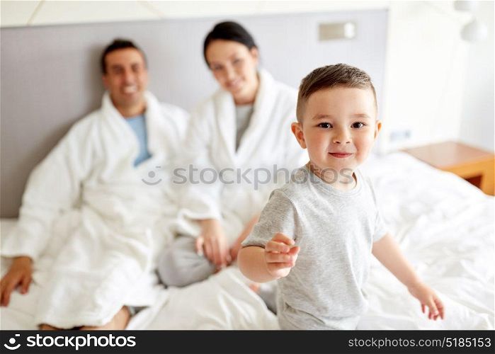people, family and morning concept - happy child with parents in bed at home or hotel room. happy family in bed at home or hotel room