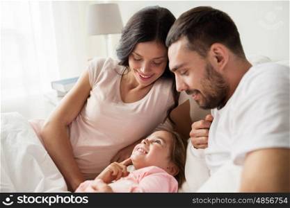 people, family and morning concept - happy child with parents in bed at home