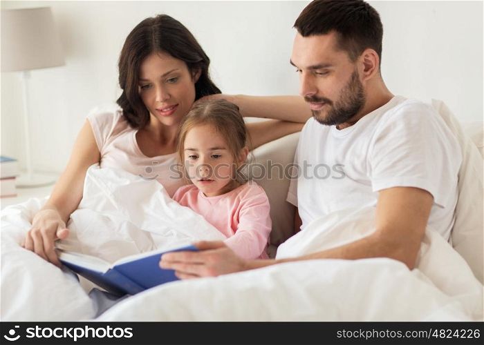 people, family and morning concept - happy child with parents reading book in bed at home