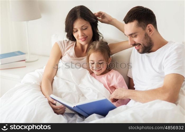 people, family and morning concept - happy child with parents reading book in bed at home