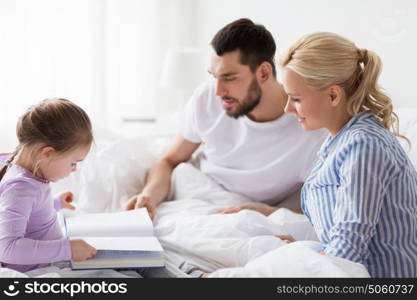 people, family and morning concept - happy child with parents reading book in bed at home. happy family reading book in bed at home