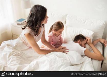 people, family and morning concept - happy child with parents waking up in bed at home
